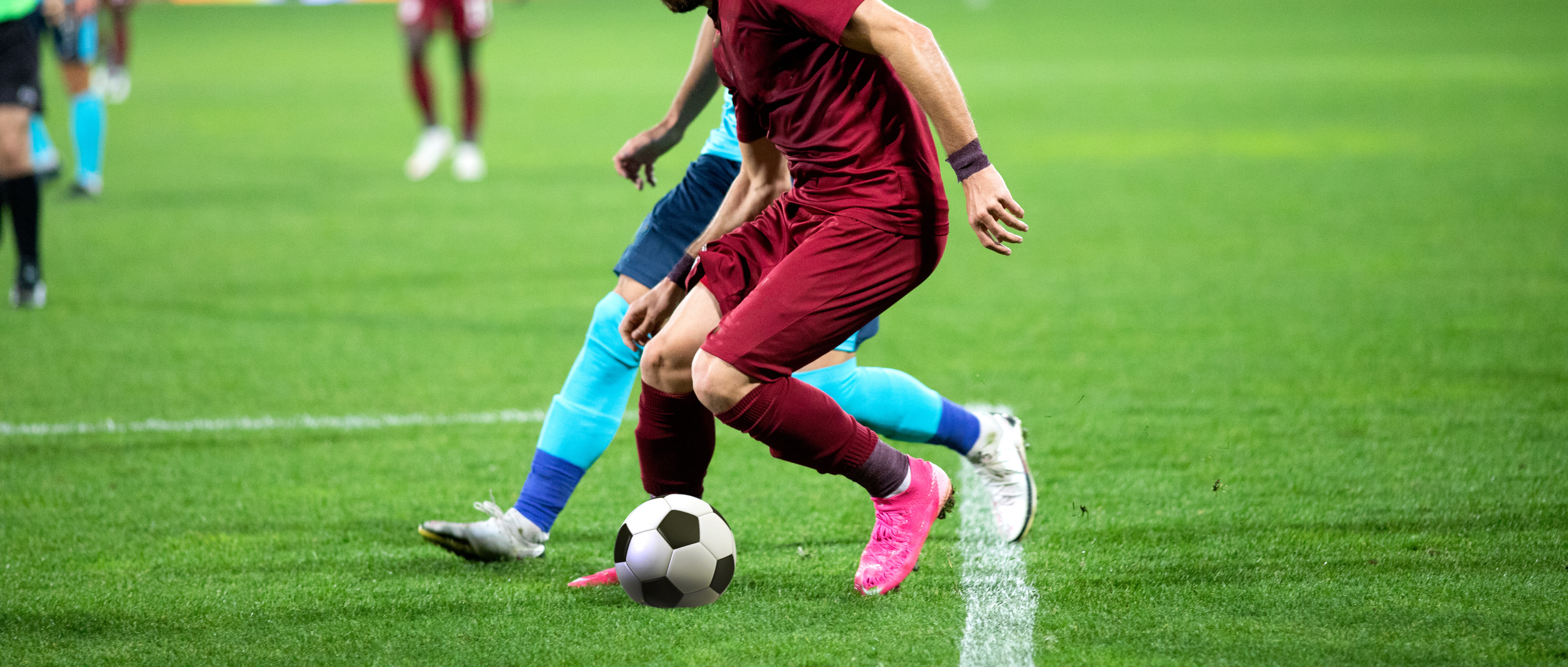 Picture of live football game, two pairs of legs from opposing teams tackling a football. 