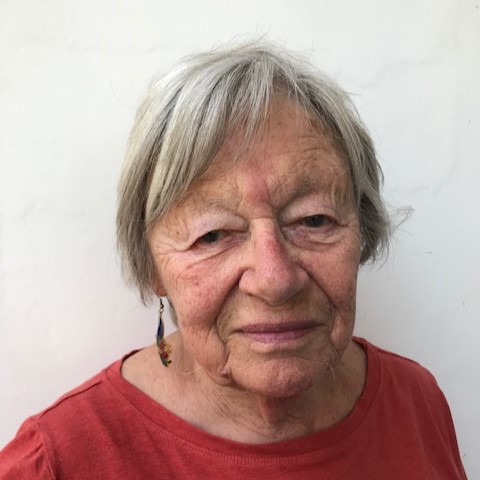 Headshot of Sheila, grinning while wearing a red top.